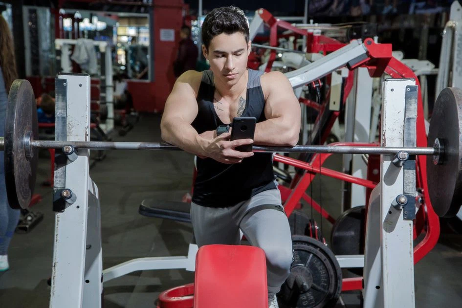 Lifter checking a free gym workout app on a phone next to a loaded barbell